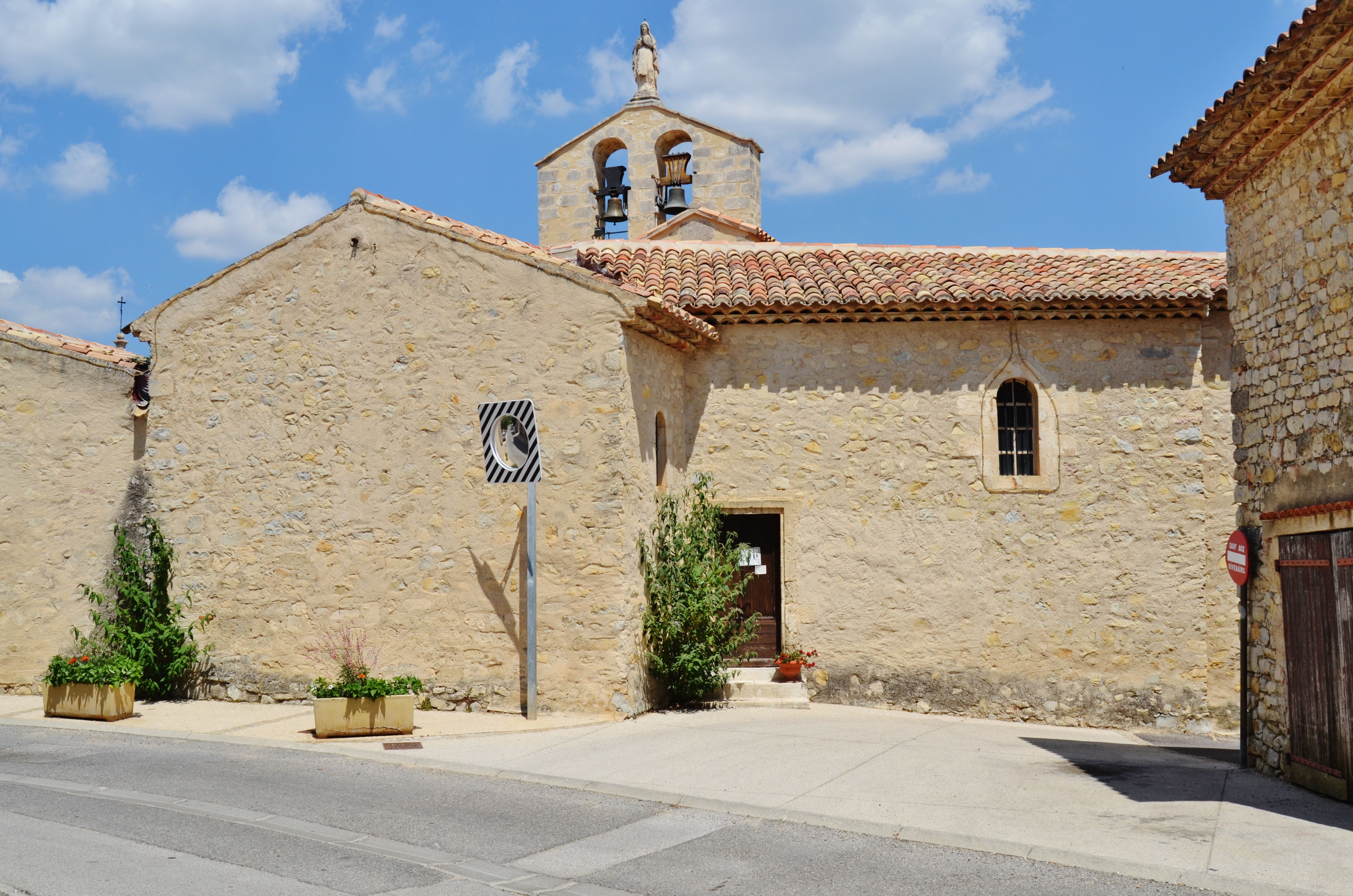 Ancient stone church in Vitrolles-en-Lubéron, Provence, under a blue sky.
