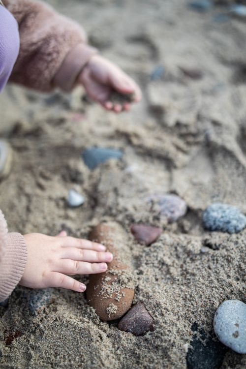 Free Close-up of a child's hands playing with stones in the sand on a beach, illustrating playful exploration. Stock Photo