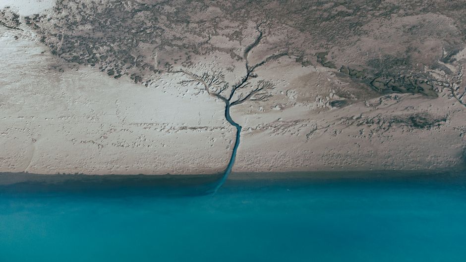 Stunning aerial view of a tranquil river delta merging with a blue body of water in Iceland's rugged landscape.