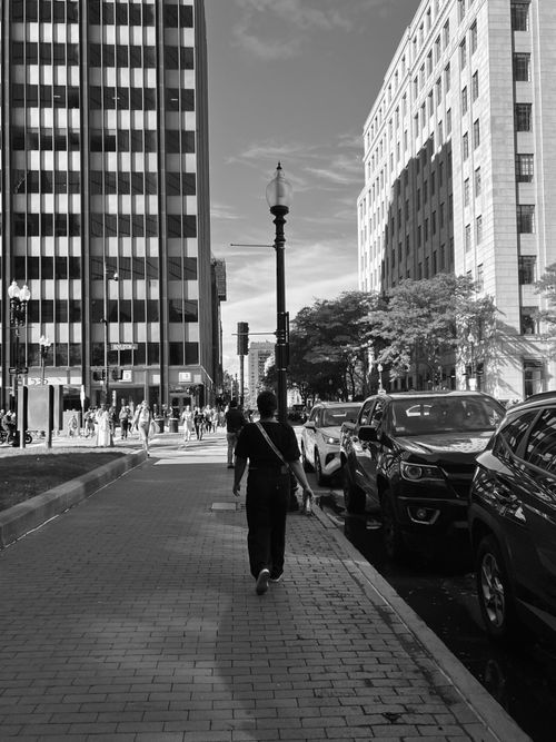 Free Monochrome city street with a lone pedestrian walking by tall buildings. Stock Photo