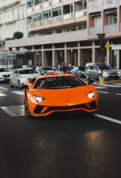 Bright orange sports car driving through a busy city street in the daytime.