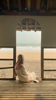 A woman in a hijab enjoys a peaceful beach view from a rustic hut in Malang, Indonesia.