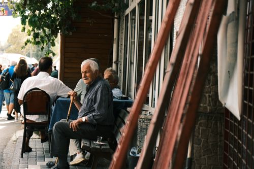 Free An elderly man with a cane sitting outdoors on a lively street corner. Stock Photo