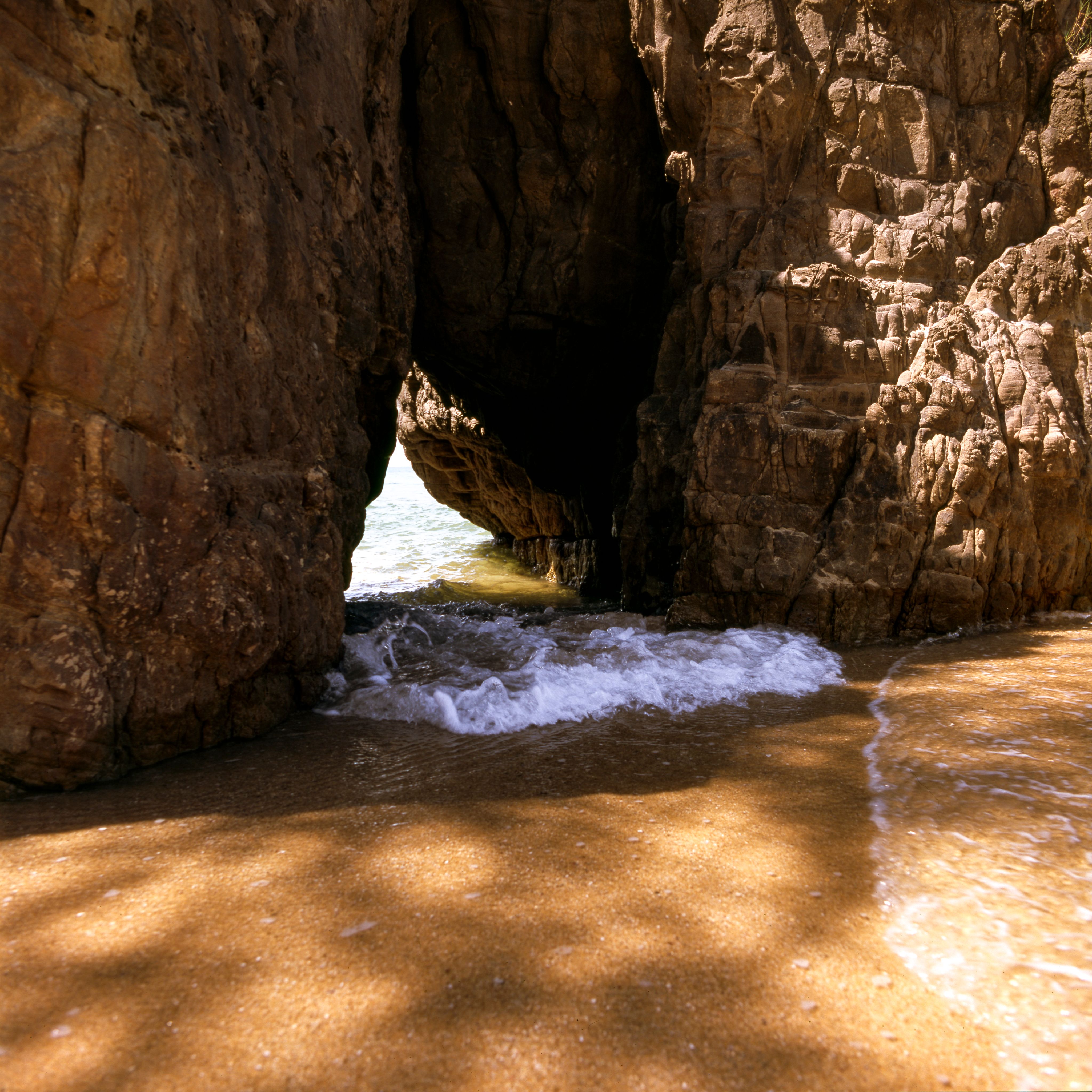 A scenic view of ocean waves flowing through a natural rock formation on a sandy beach.