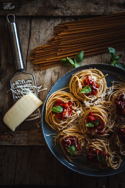 Rustic presentation of spaghetti with tomatoes, basil, and grated cheese on wooden table.