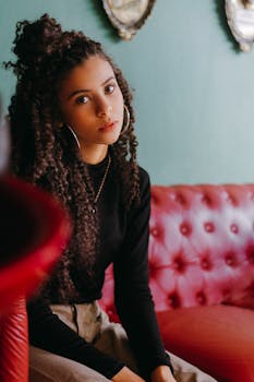 一位卷发的年轻女子坐在室内红色沙发上，肖像时尚而休闲