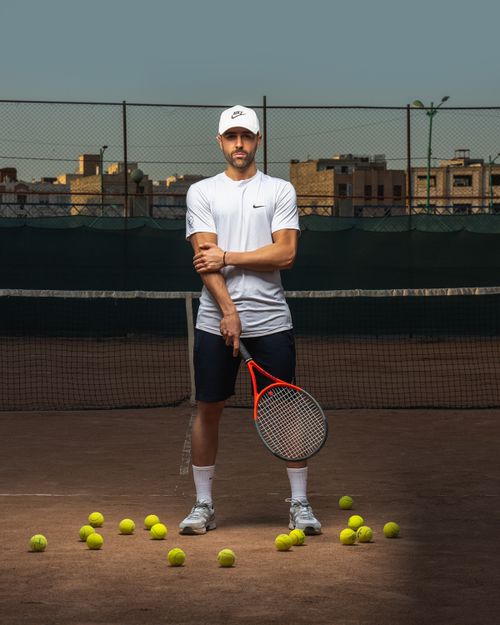 Free Portrait of a professional tennis player standing confidently on a clay court with tennis balls scattered around. Stock Photo