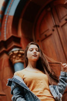 一位穿着休闲服的时尚年轻女子，以低视角对着一扇精致华丽的木门摆姿势