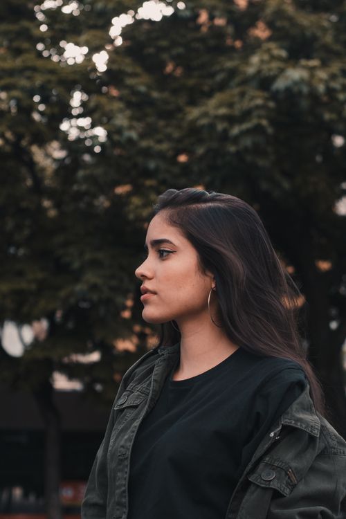 Free Portrait of a woman with long hair in casual wear standing outdoors among trees. Stock Photo