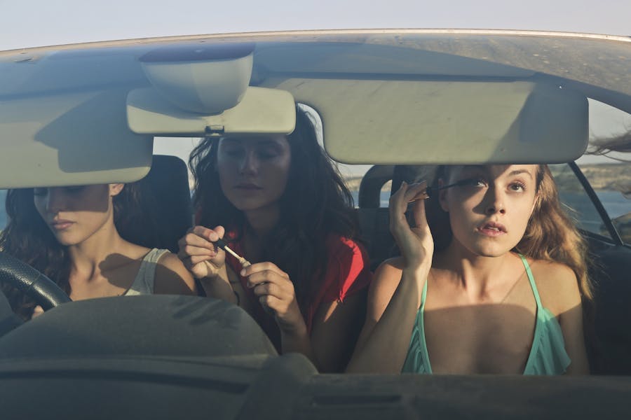 Trois jeunes femmes covoiturent dans une décapotable, se maquillant