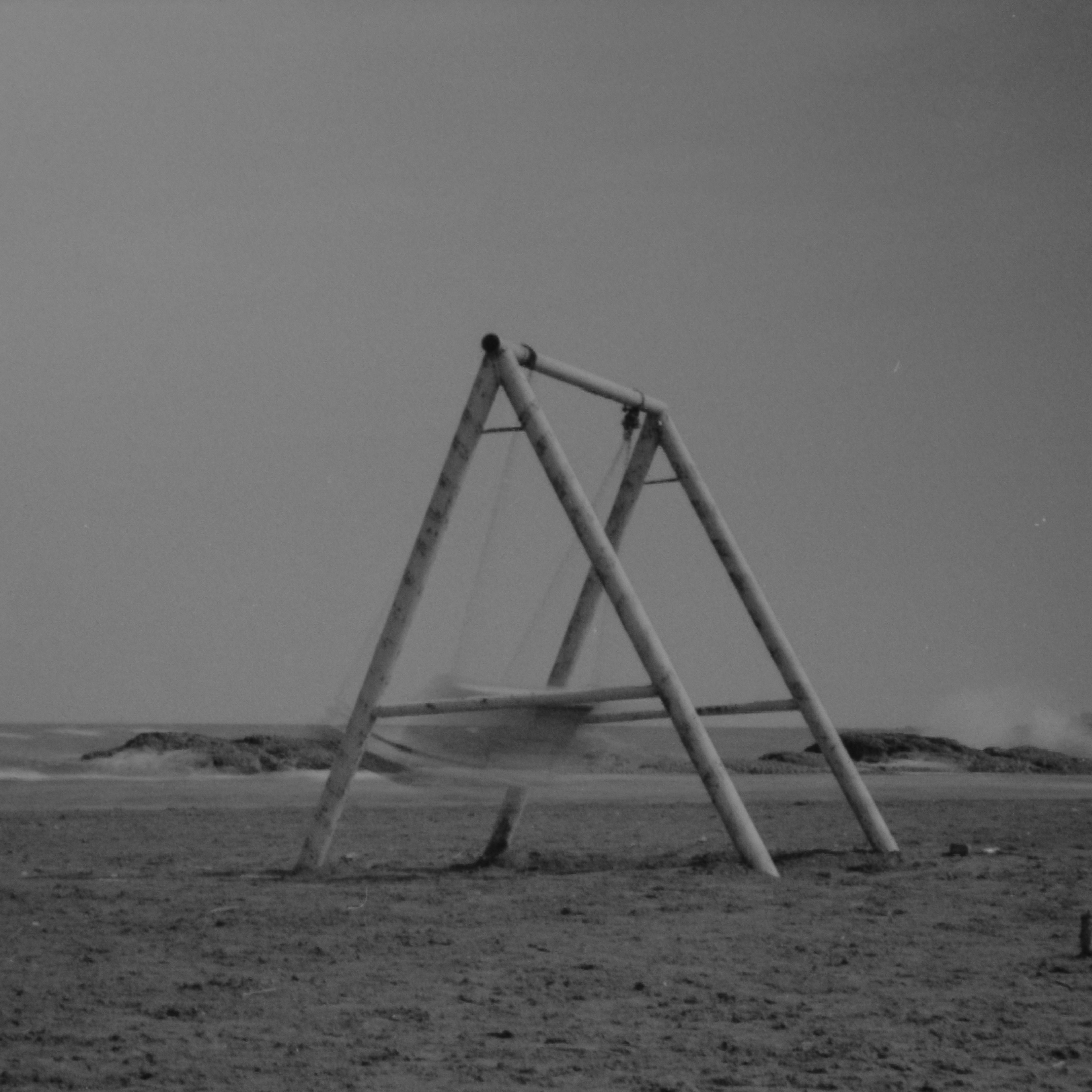 Black and white image of a swing set on an empty beach, evoking solitude.