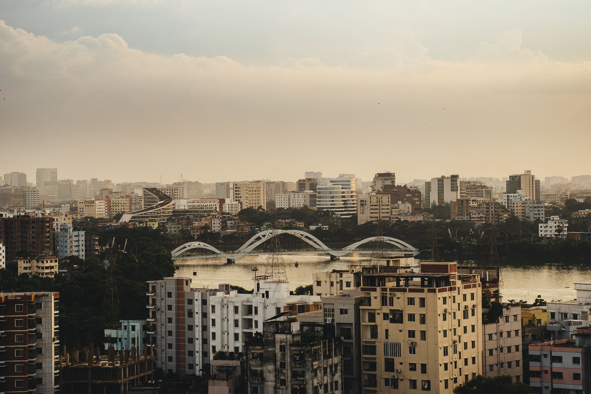 Aerial view of Dhaka city skyline with bridge over river at sunset.