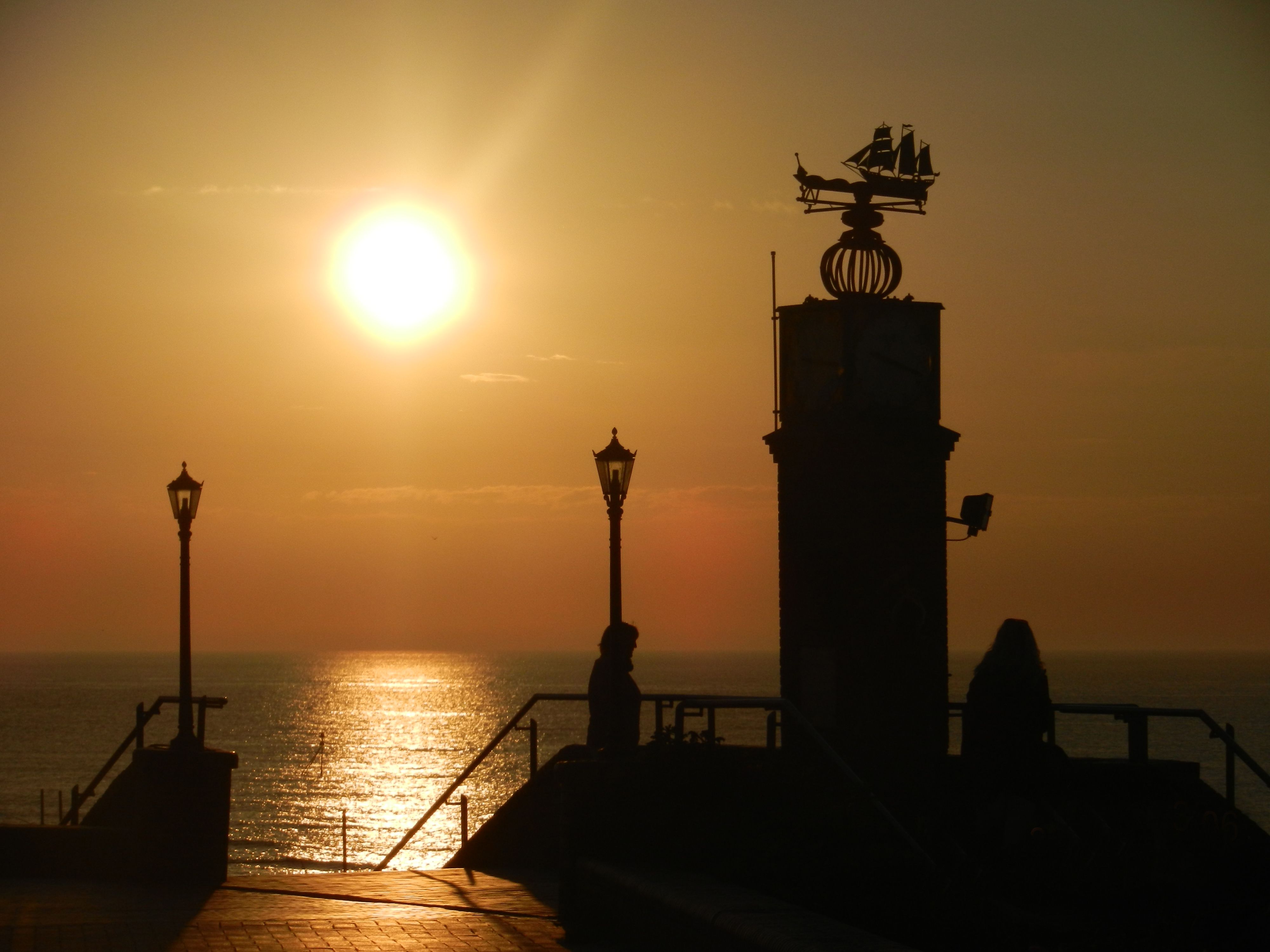 Silhouetted promenade lamps and people beside the sea at sunset in Aberystwyth, United Kingdom