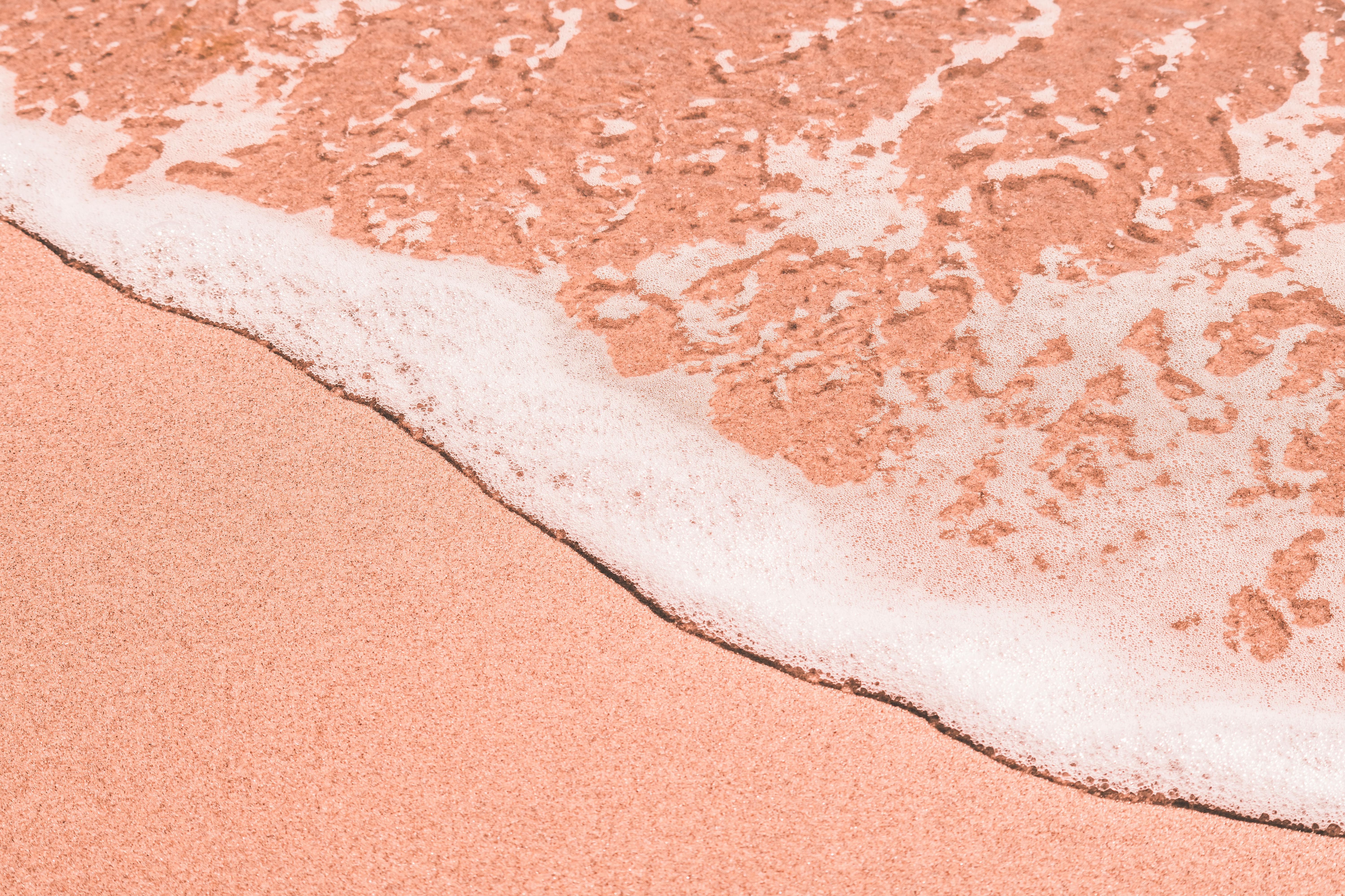 粉红色的沙滩特写中，柔和的海泡沫侵蚀着海岸，营造出宁静的沿海风光