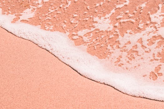 粉红色的沙滩特写中，柔和的海泡沫侵蚀着海岸，营造出宁静的沿海风光