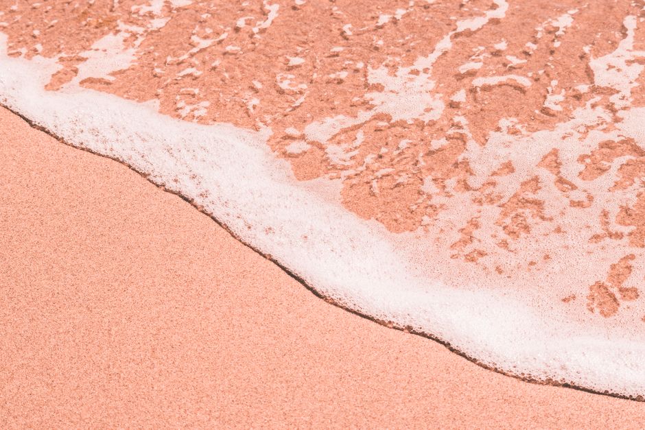 Close-up of a pink sandy beach as gentle sea foam encroaches on the shore, creating a tranquil coastal scene.