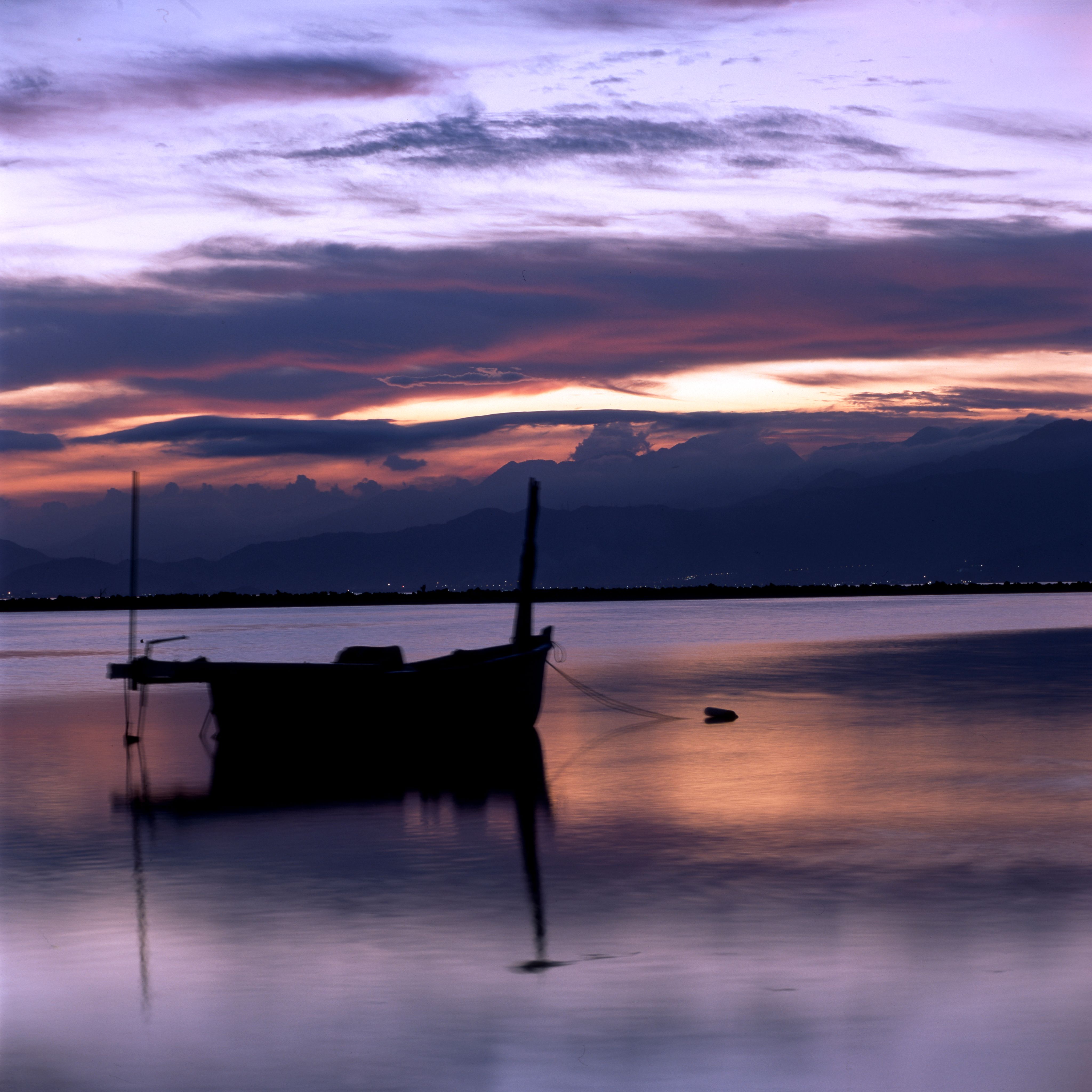 A peaceful sunset scene with a silhouetted boat on a tranquil lake, reflecting colorful skies.