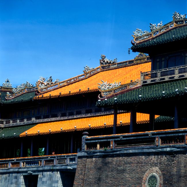 A traditional Asian temple with ornate green and orange roofs against a bright blue sky.