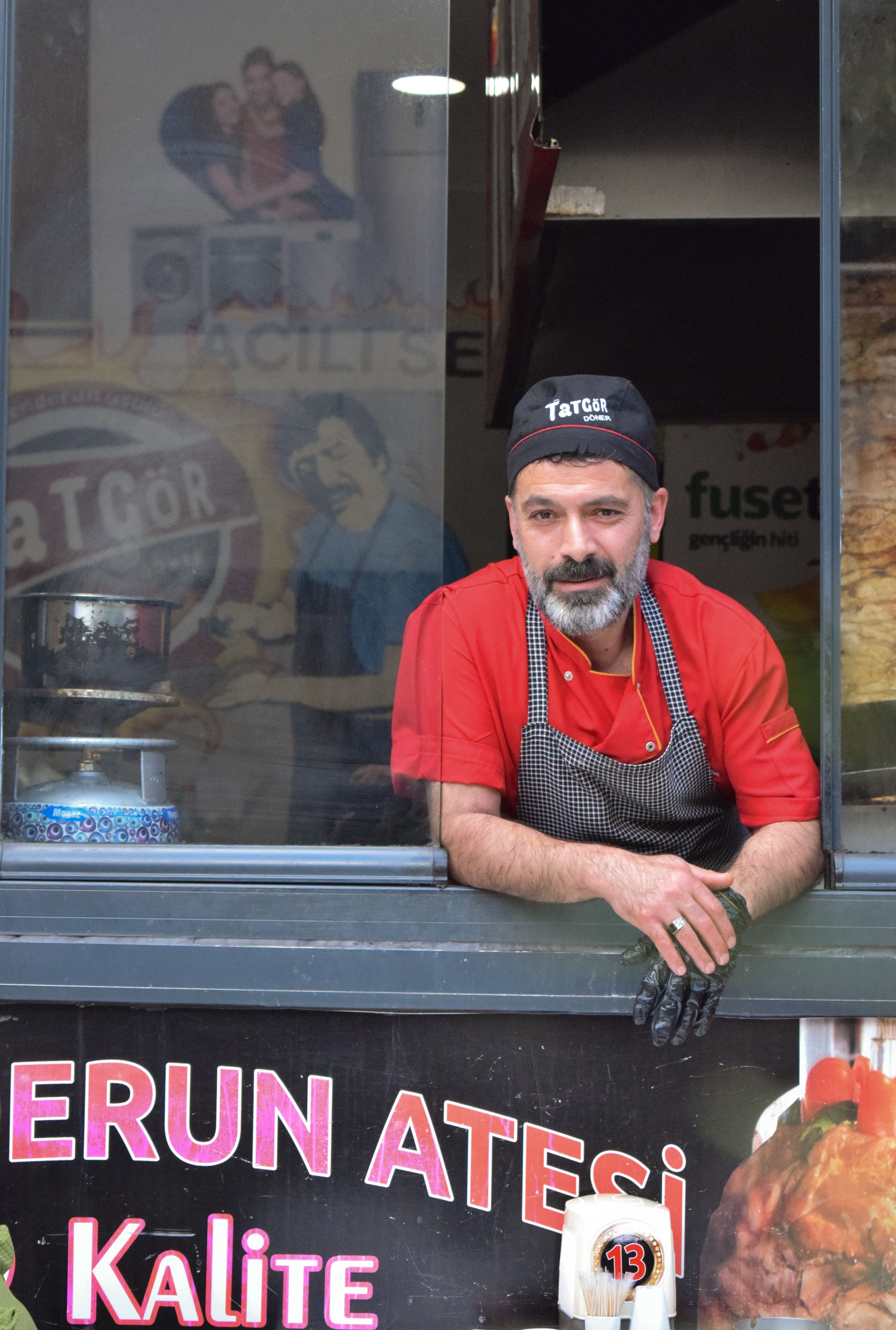 Chef in red uniform leaning from a kitchen window in a restaurant setting. Street photography style.