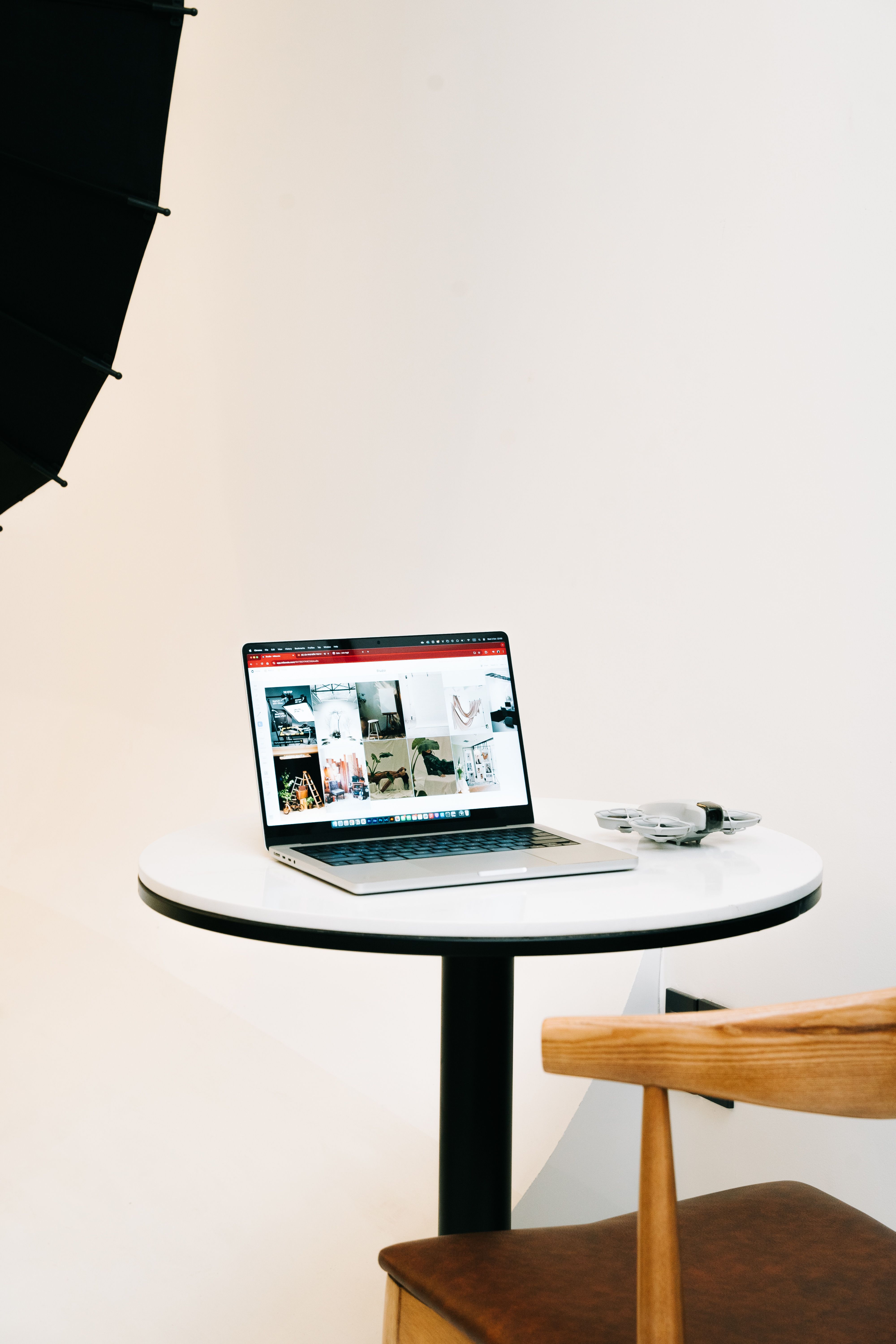 A clean, minimalist workspace with a laptop displaying various images on a round table and a modern chair nearby.