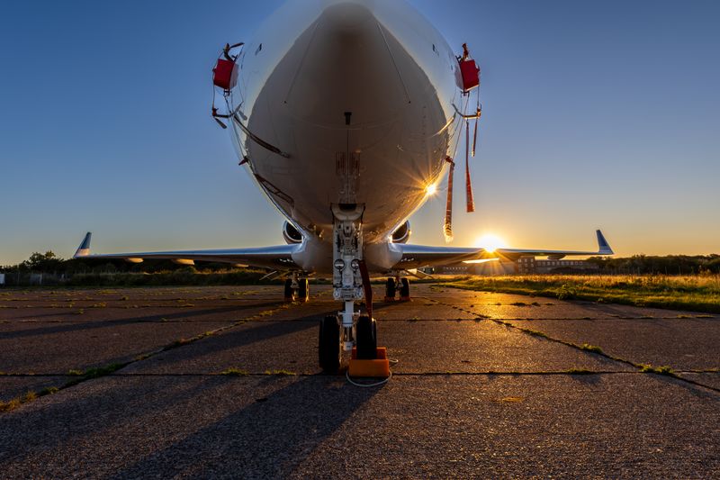 Close-up of airplane parked outdoors on runway during sunset, highlighting aviation theme.