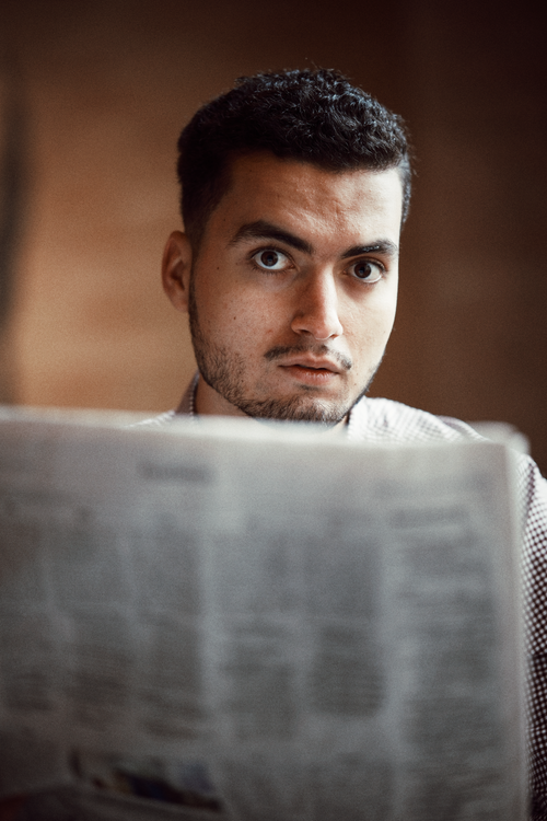 Free Focused young man reading a newspaper with an intense gaze indoors. Stock Photo