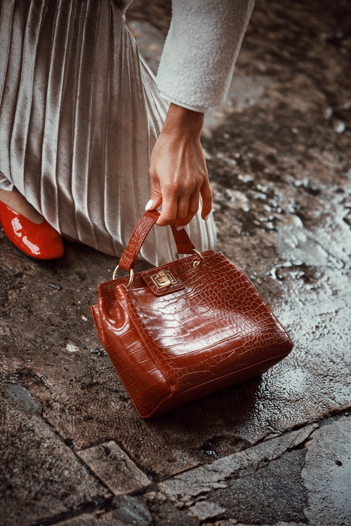 Free Elegant hand holding a red handbag on wet cobblestone, exuding classic fashion sense. Stock Photo