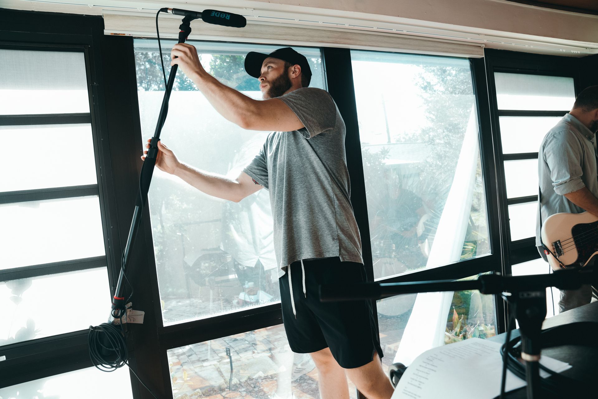 A man adjusts a boom microphone indoors during a video production setup.