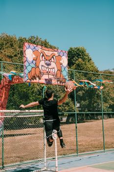 A male basketball player dunking on an outdoor court in Brasília, showcasing athletic skill and vibrant graffiti art.