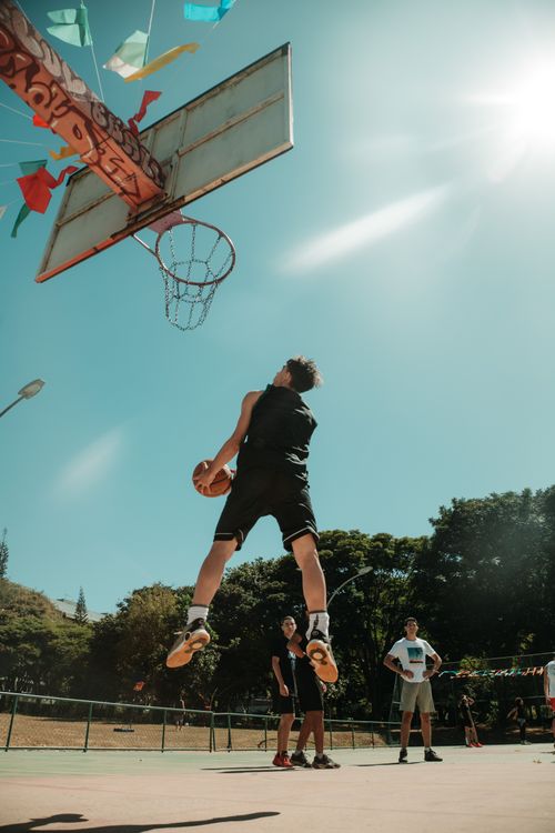 Free Energetic street basketball scene in Brasília capturing a thrilling dunk against a clear blue sky. Stock Photo