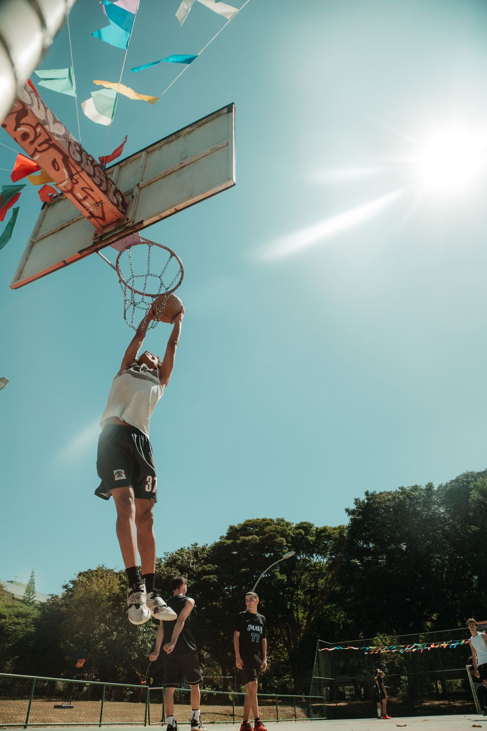Athlete mid-air dunking under a bright blue sky on an outdoor court