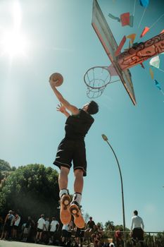Athlete jumps for a basketball dunk under a bright sky on a vibrant outdoor court in Brasília.