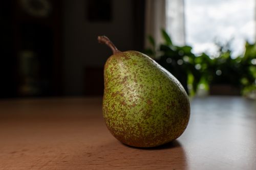 Free A close-up image of a ripe green pear placed on a wooden table with soft natural lighting. Stock Photo