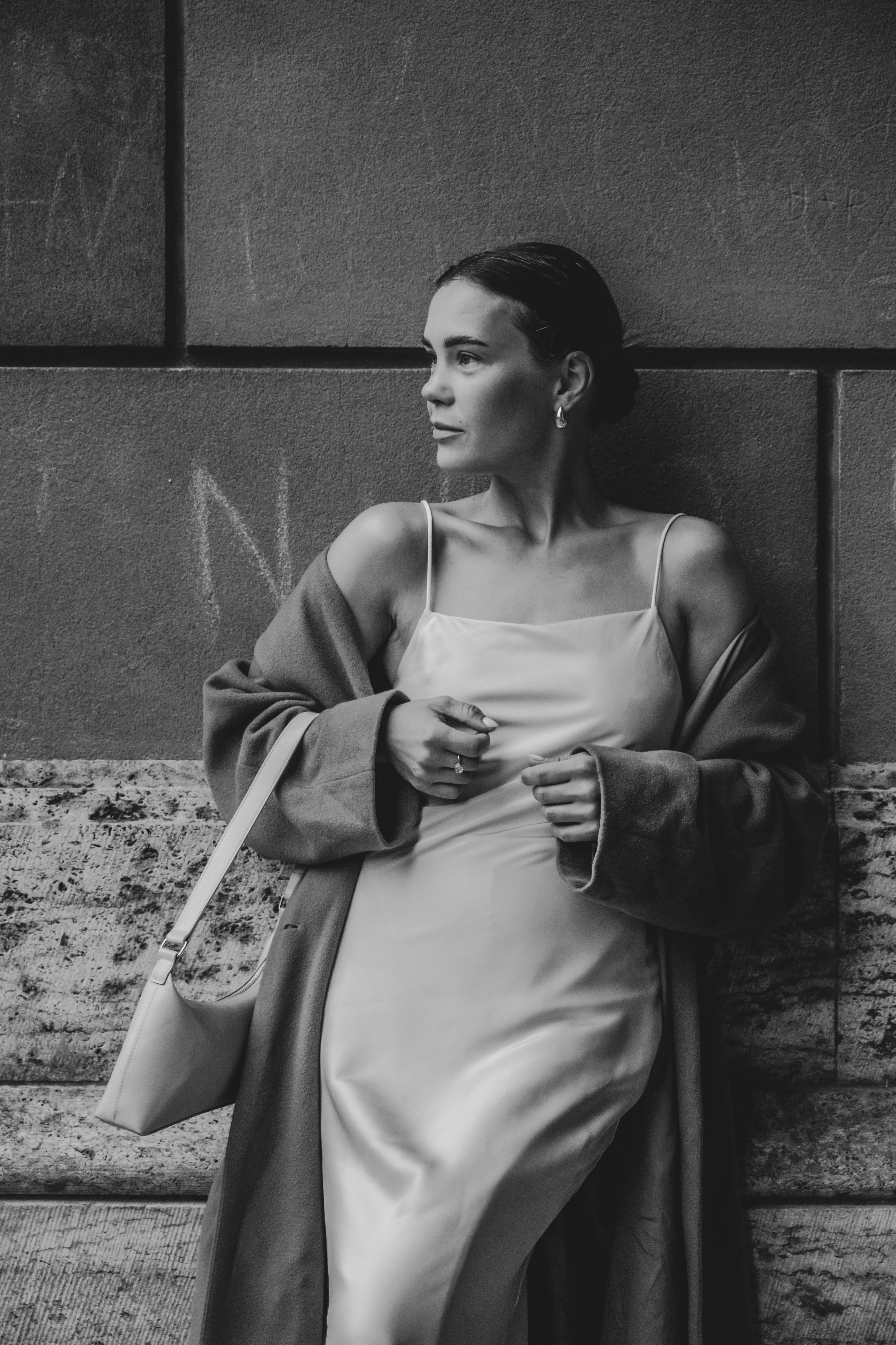 Black and white portrait of a stylish woman leaning against a wall.