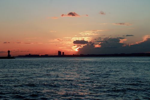 Free Serene sunset over the ocean with distant city skyline and lighthouse. Stock Photo