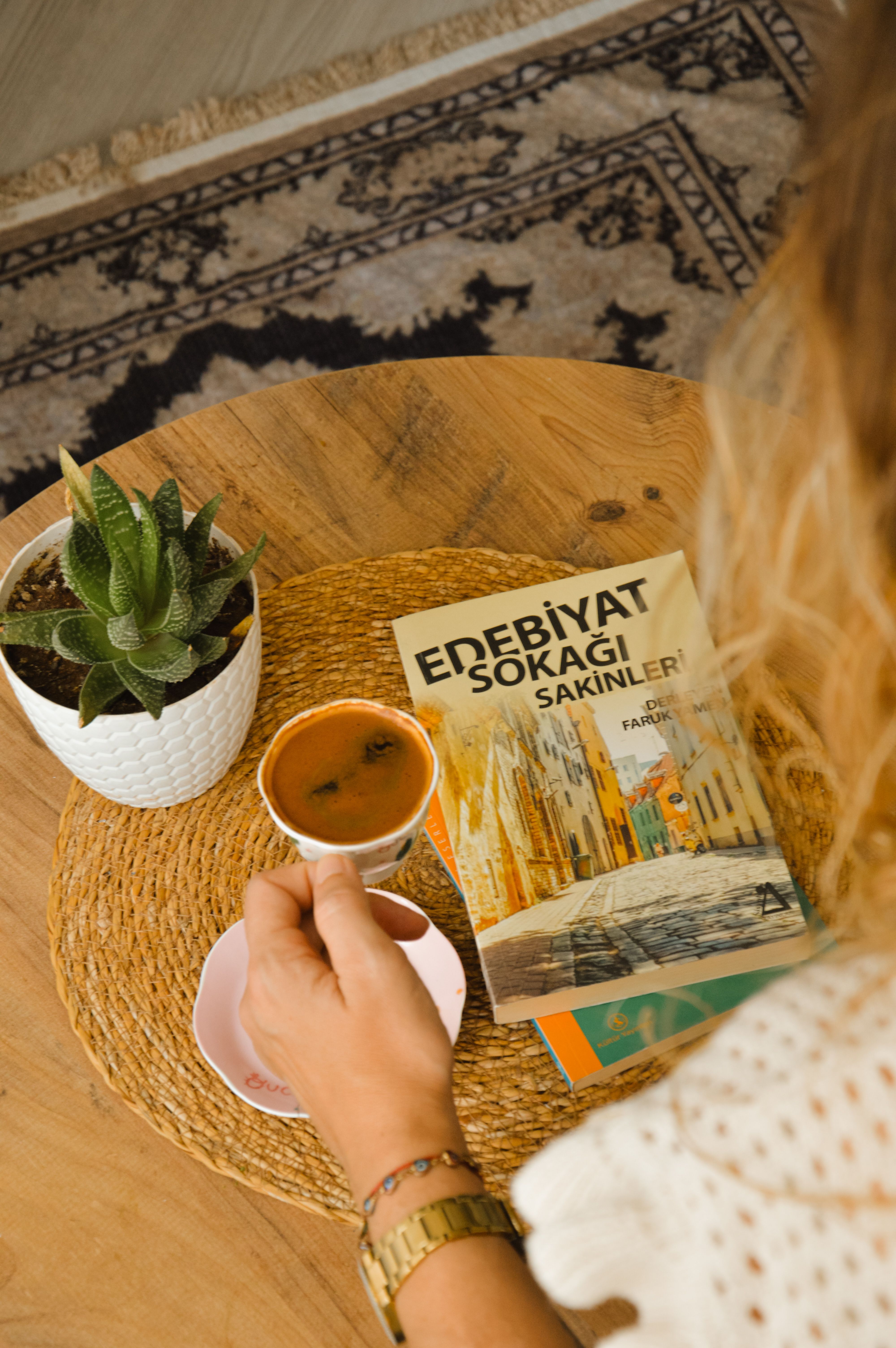 A cozy setup with coffee, a book, and a potted plant on a wooden table.