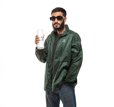 Stylish man in a green jacket with sunglasses holding a branded bottle.