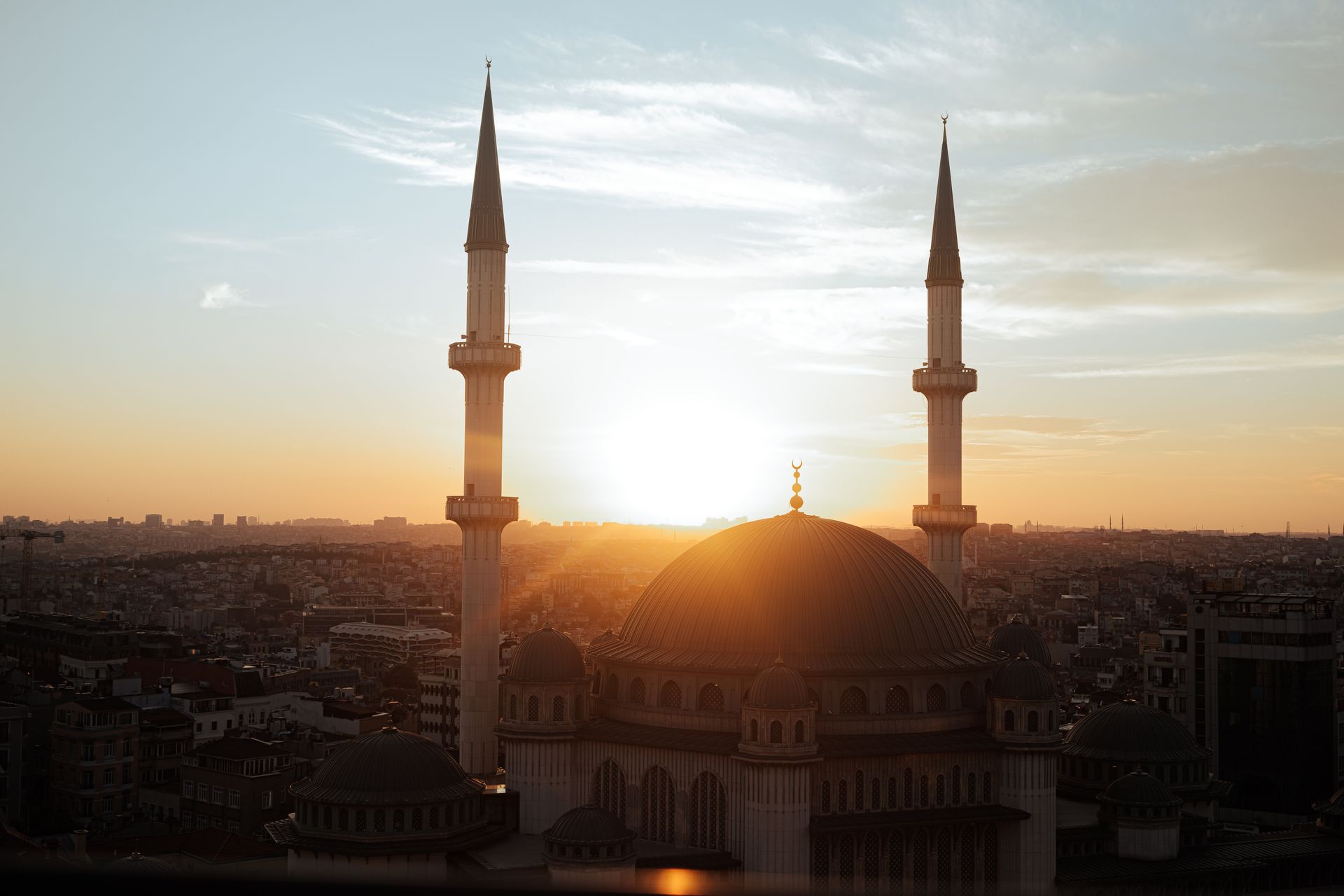 A stunning view of a mosque with tall minarets at sunset, overlooking a bustling cityscape.