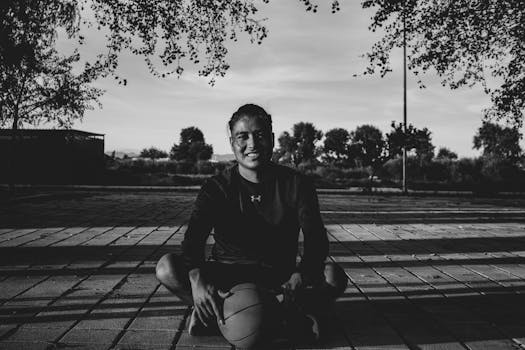 A young basketball player smiles while seated outdoors with a basketball in black and white.