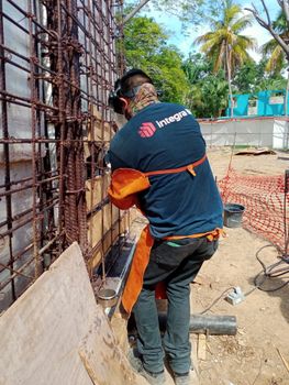 Worker welding on rebar at a construction site under a bright sun.