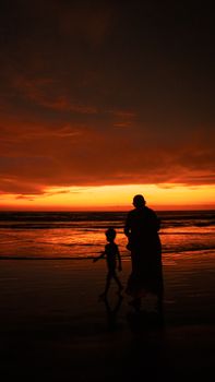 A serene silhouette of an adult and child walking on a beach at sunset, capturing the vibrant hues and serene moment.
