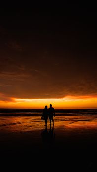 Romantic silhouette of a couple walking along a beach during a dramatic sunset.