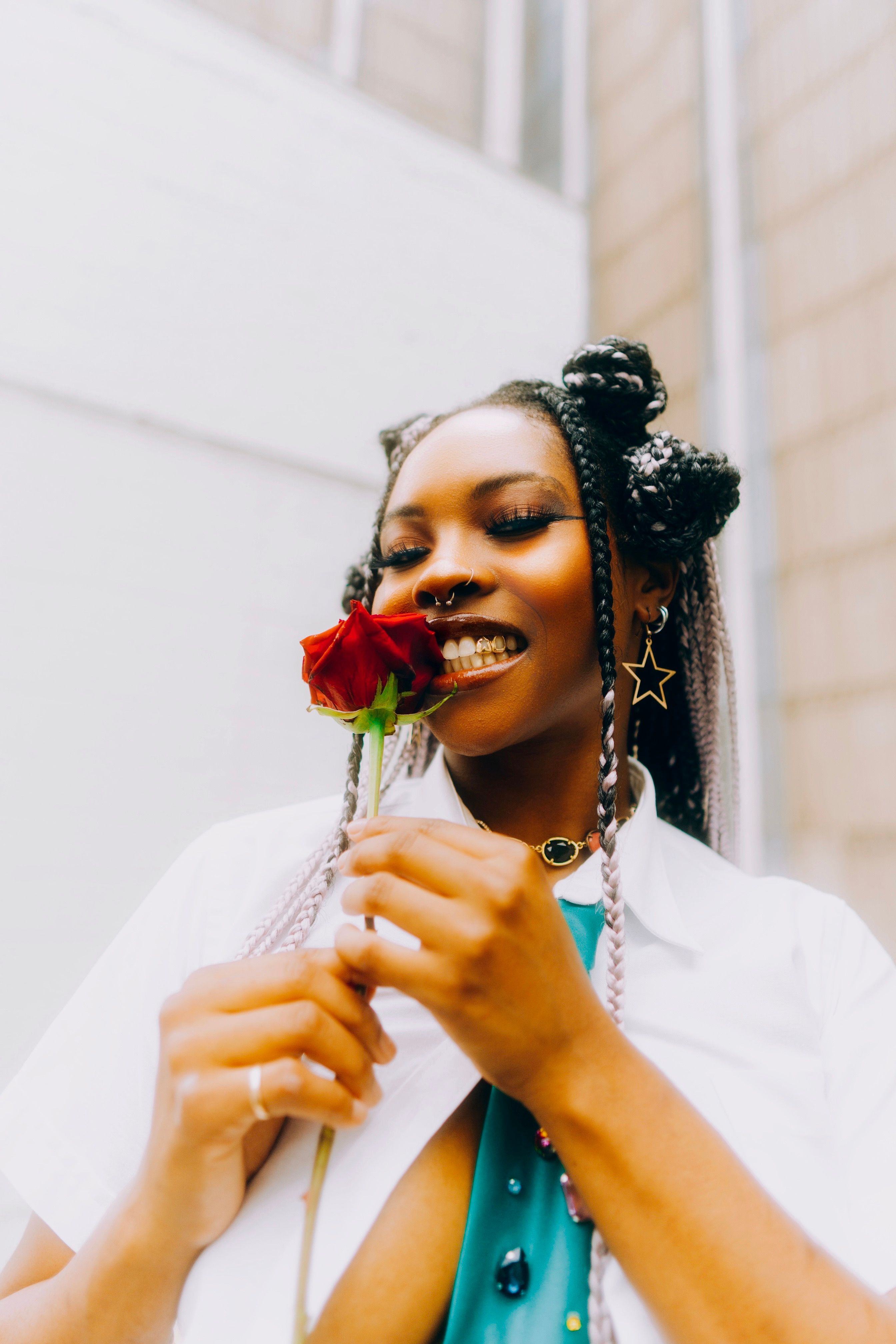 A woman with Afro braids smiles while holding a red rose, showcasing her unique style.