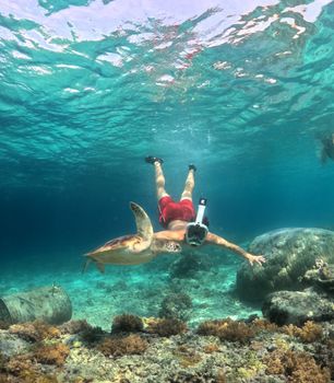 A snorkeler swimming alongside a sea turtle in clear tropical waters.