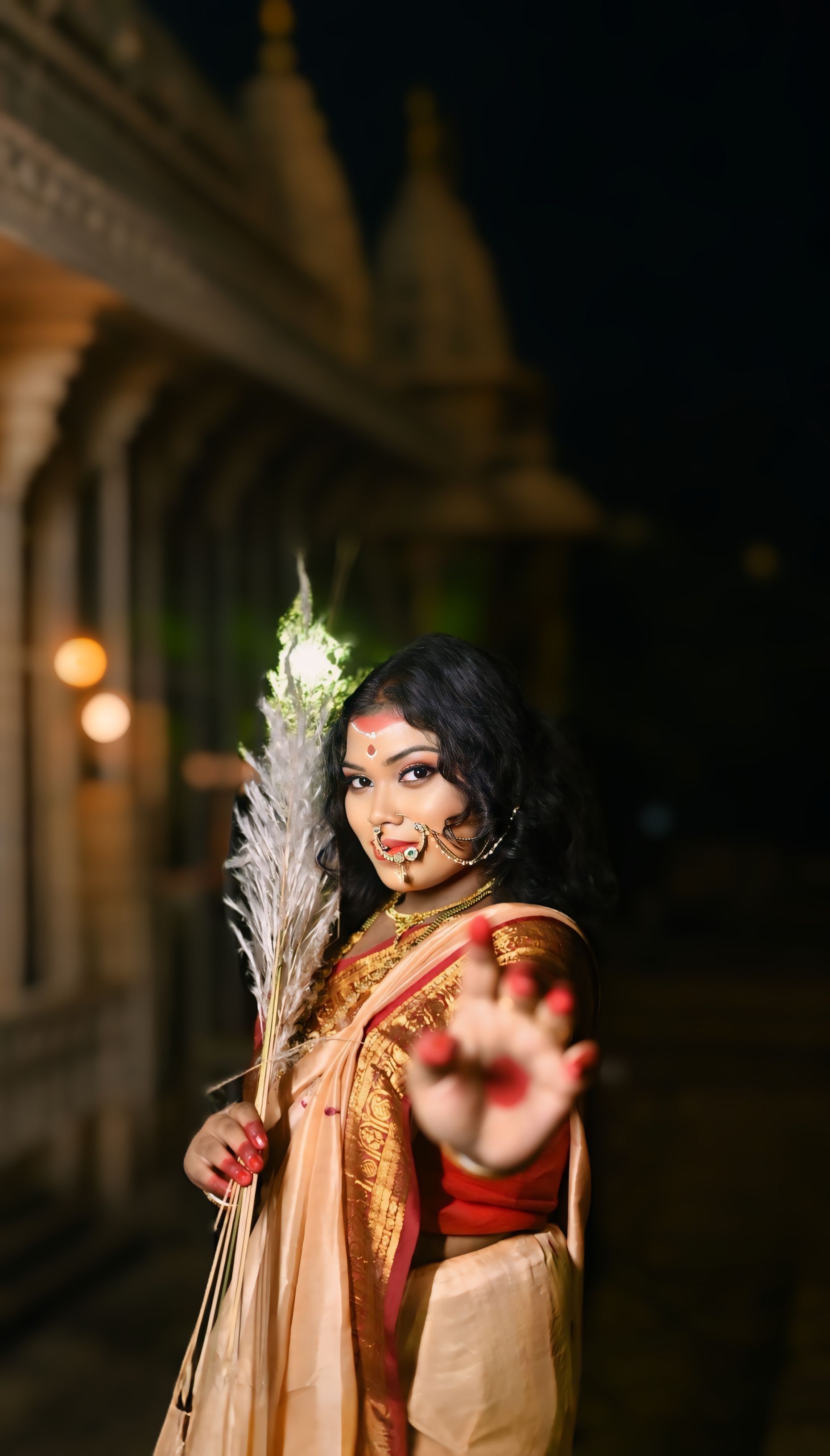 A woman in traditional attire celebrates Durga Puja at night, showcasing cultural heritage.