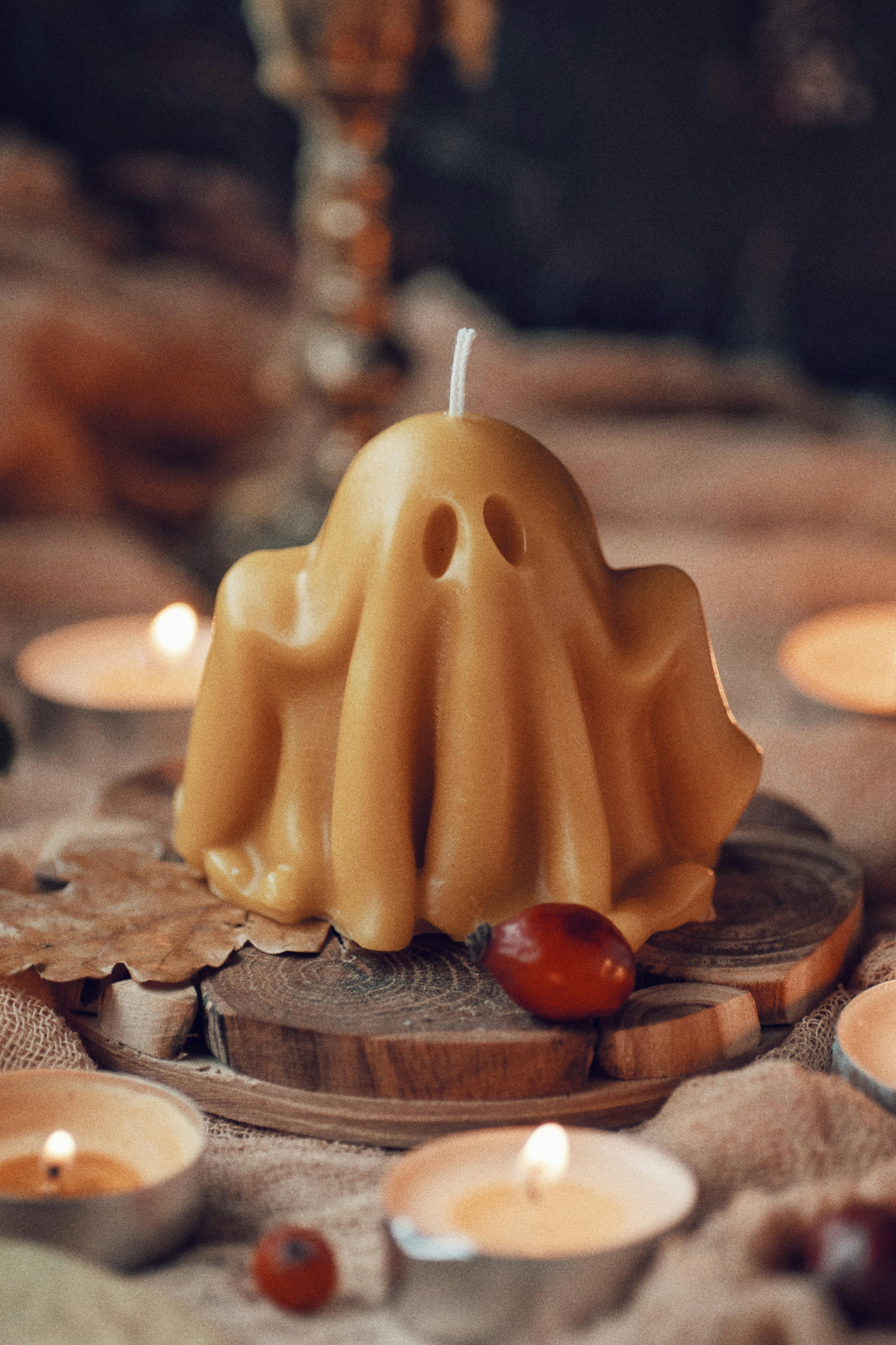 A spooky ghost-shaped candle surrounded by warm autumn decor and lit candles.