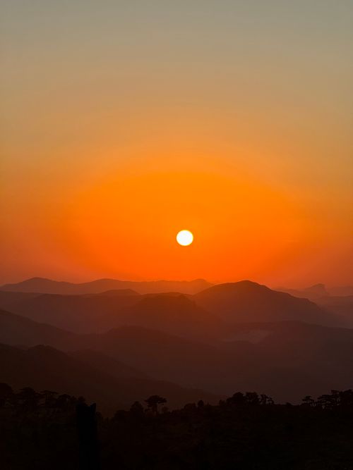 Free Serene sunset over hazy mountains with vibrant orange sky, offering a tranquil view. Stock Photo