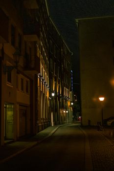 Peaceful narrow city street at night illuminated by warm streetlights creating a moody ambiance.