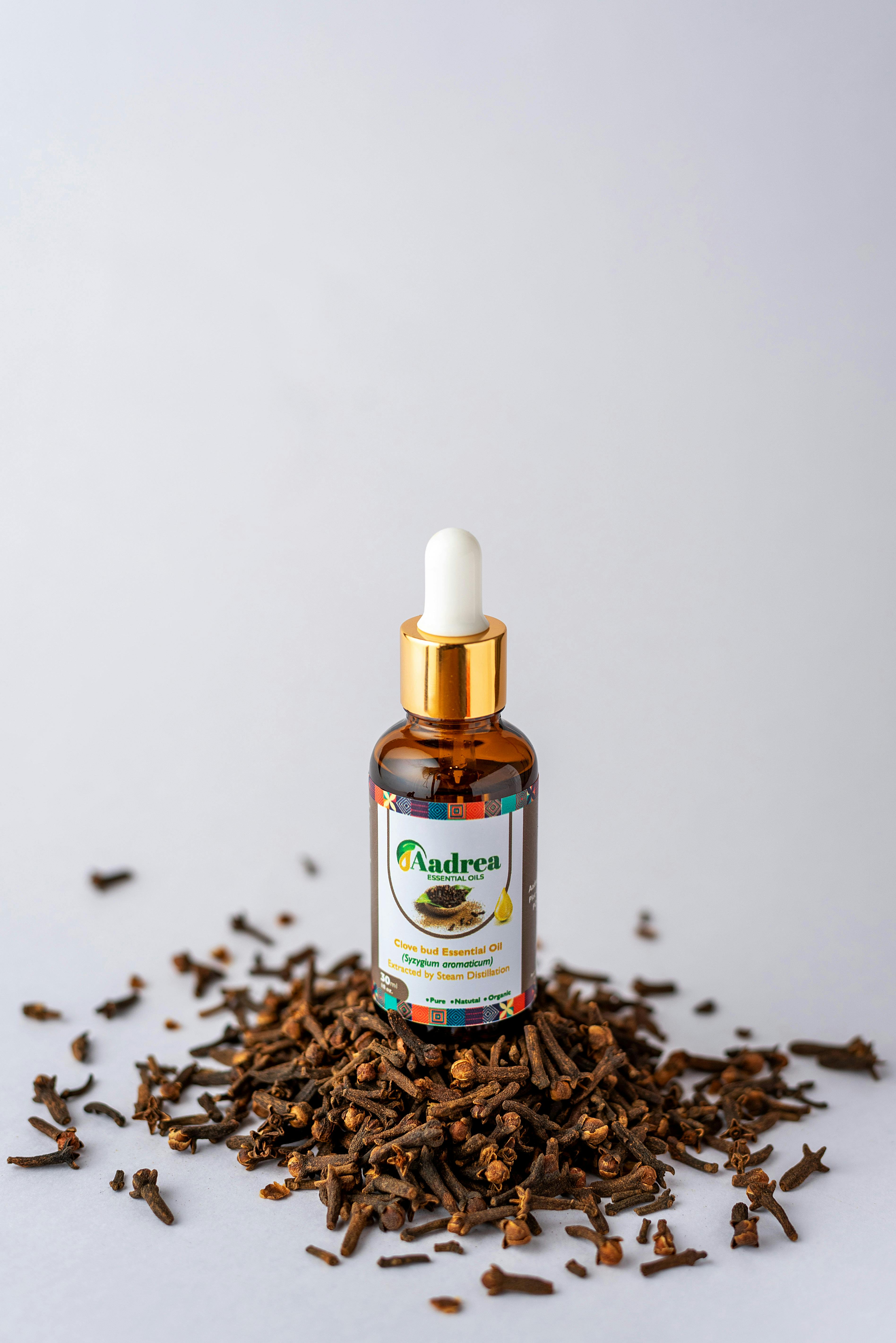 Brown glass bottle of clove essential oil surrounded by clove buds on a white background.