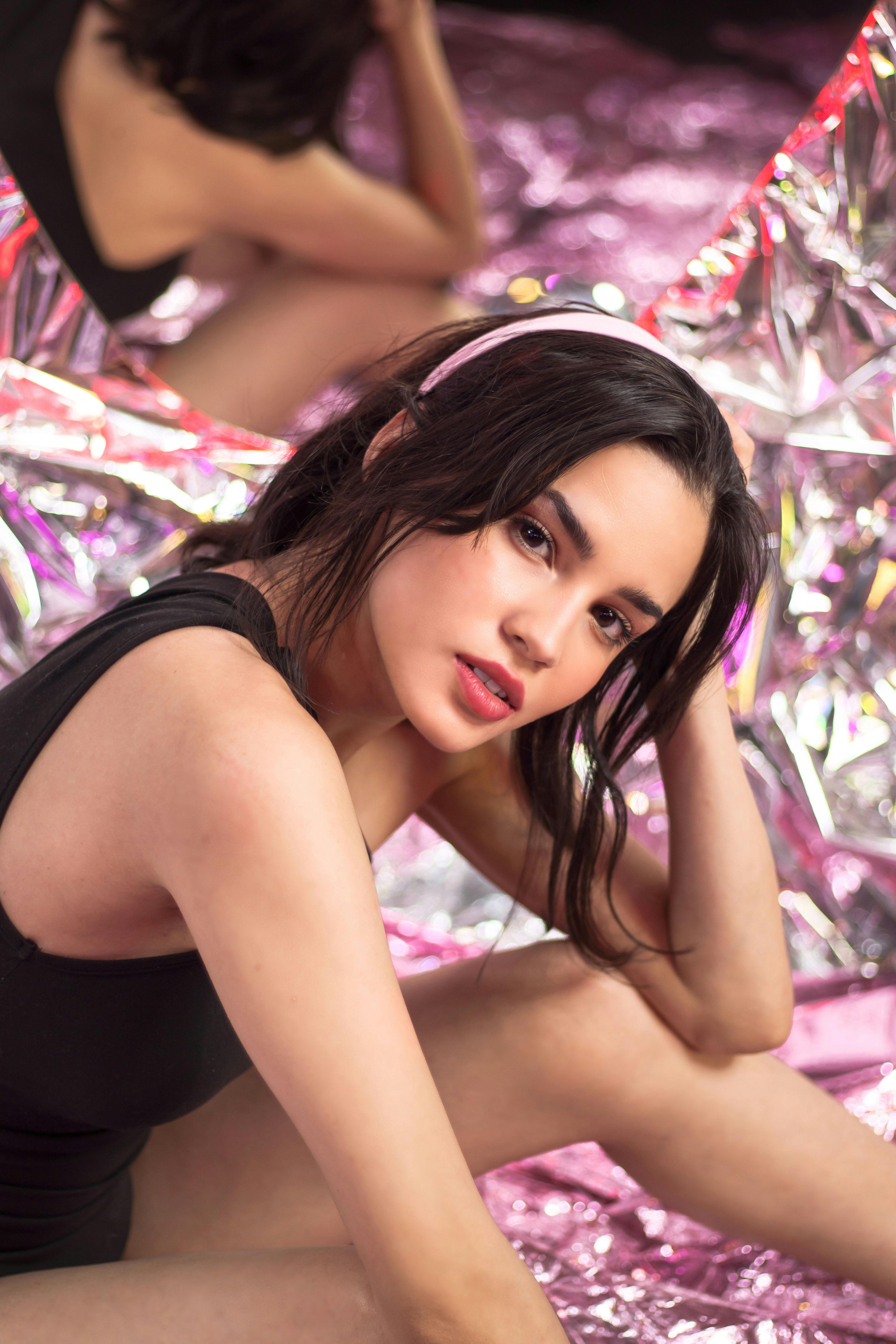 Young woman posing in front of a reflective backdrop with a vibrant, stylish ambiance.